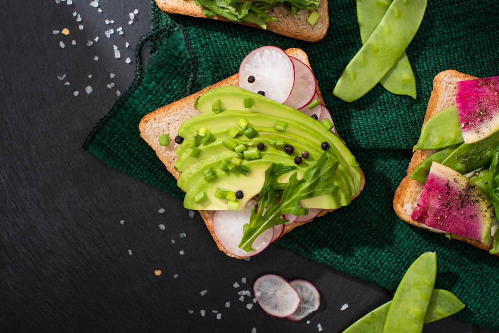 vista superior de tostadas frescas con rábano y aguacate sobre tela verde
 - Foto, imagen