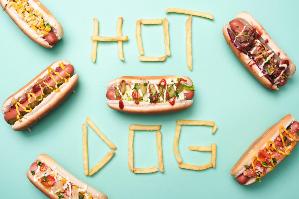 vista superior de perritos calientes poco saludables en azul con palabra hot dog hecha de papas fritas
  - Foto, imagen