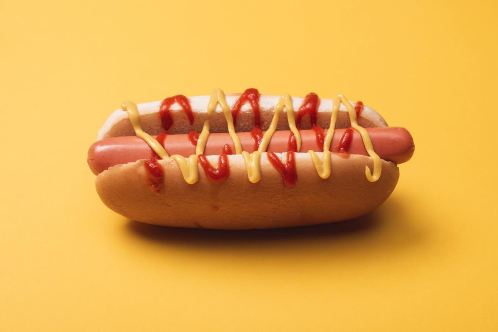 perrito caliente poco saludable con salchicha, mostaza y ketchup en amarillo
  - Foto, imagen