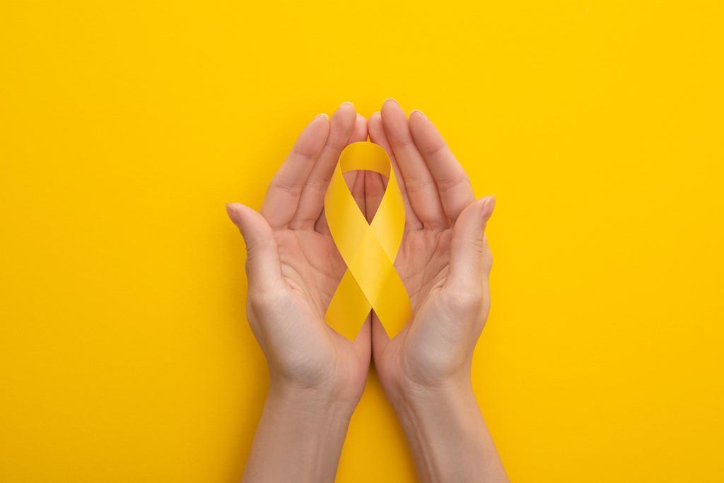 Teilansicht weiblicher Hände mit gelbem Band auf buntem Hintergrund, Konzept zum internationalen Kinderkrebstag - Foto, Bild