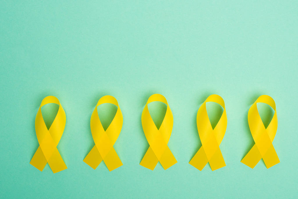 Acostado plano con cintas de conciencia amarillas sobre fondo turquesa, concepto de día internacional del cáncer infantil
 - Foto, Imagen