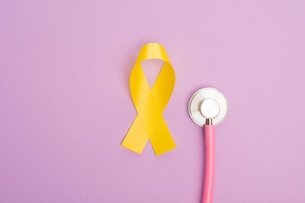 Vue du dessus du ruban jaune avec stéthoscope sur fond violet, concept de journée internationale contre le cancer chez l'enfant
 - Photo, image