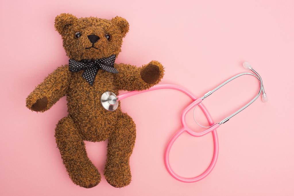 Top view of stethoscope connected with teddy bear on pink background, international childhood cancer day concept - Photo, Image