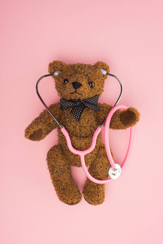 Κάτοψη του αρκουδάκι με στηθοσκόπιο σε ροζ φόντο, διεθνής ιδέα για την ημέρα του παιδικού καρκίνου - Φωτογραφία, εικόνα