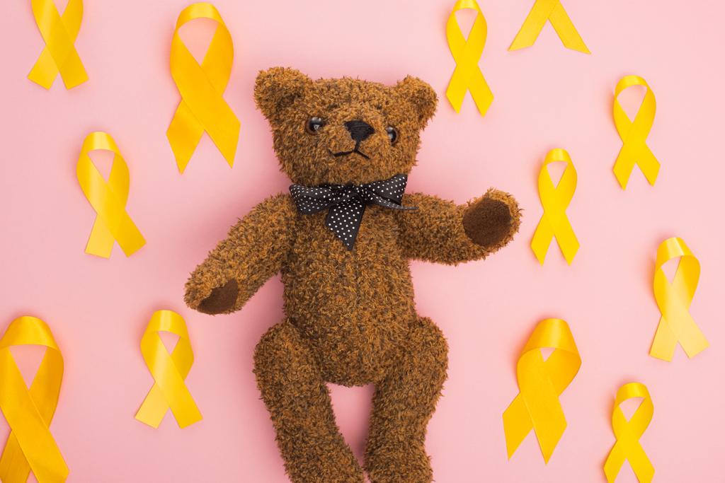 Top view of yellow ribbons around teddy bear on pink background, international childhood cancer day concept - Photo, Image