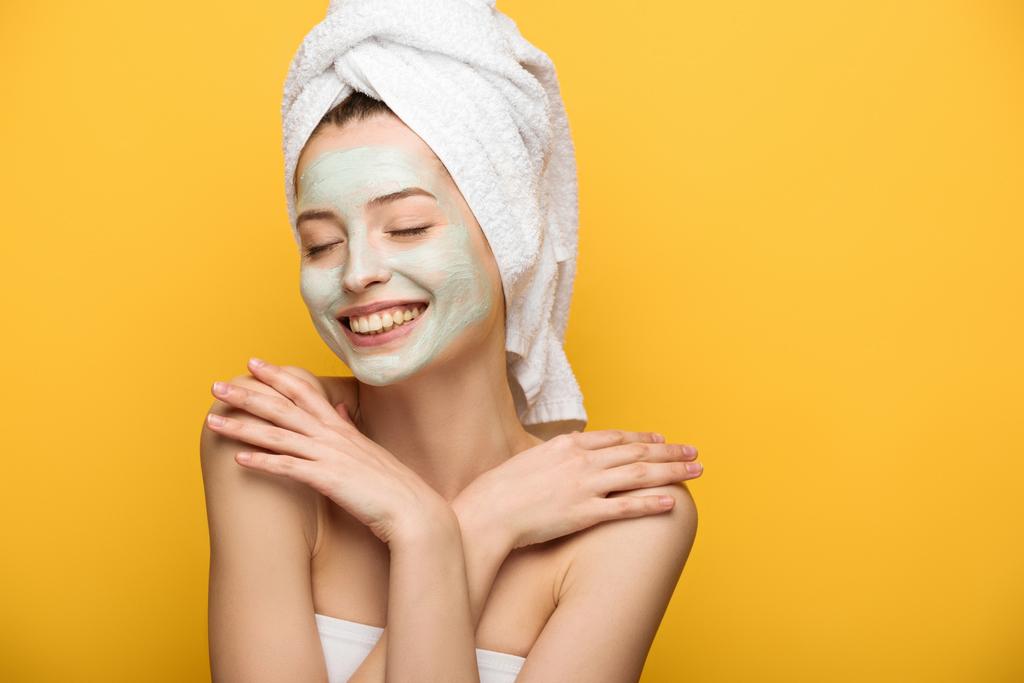 happy girl with nourishing facial mask hugging herself with closed eyes isolated on yellow - Photo, Image