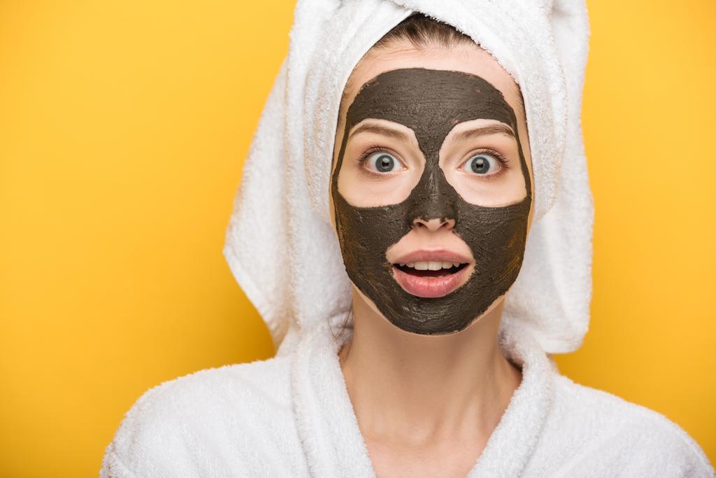 shocked girl with facial clay mask and towel on head looking at camera on yellow background - Photo, Image