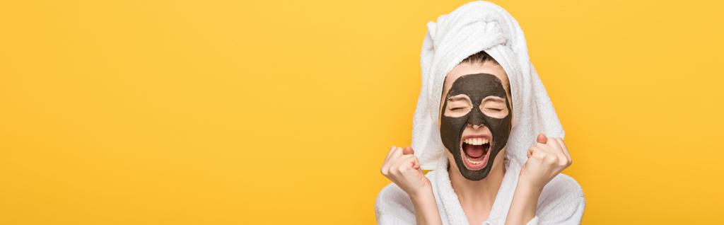 plan panoramique de fille en colère avec masque d'argile faciale et serviette sur la tête tenant les poings serrés et criant isolé sur jaune
 - Photo, image