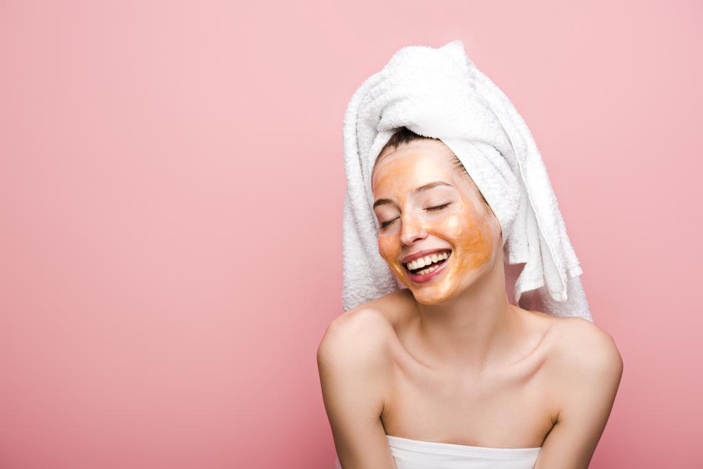 cheerful girl with facial mask and towel on head smiling with closed eyes isolated on pink - Photo, Image