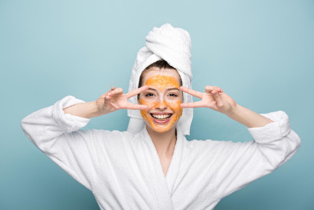 cheerful girl with citrus facial mask showing victory gestures on blue background - Photo, Image