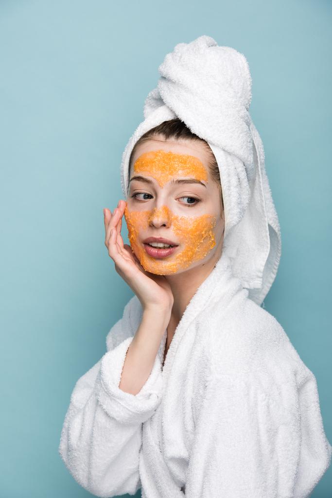 pensive girl with citrus facial mask touching face isolated on blue - Photo, Image