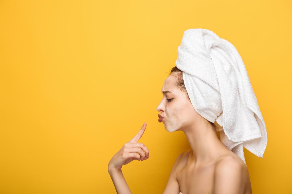 side view of girl with moisturizing facial mask pointing with finger at lips on yellow background - Photo, Image