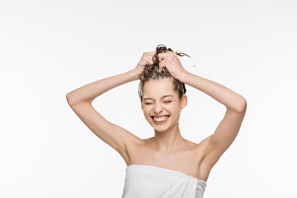 χαρούμενο κορίτσι χαμογελά με κλειστά μάτια, ενώ το πλύσιμο των μαλλιών απομονώνονται σε λευκό - Φωτογραφία, εικόνα