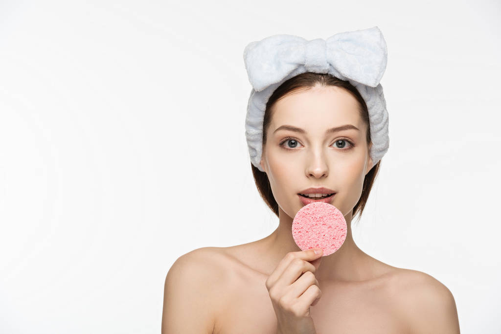 mooi meisje holding cosmetische spons in de buurt van lippen terwijl kijken naar camera geïsoleerd op wit - Foto, afbeelding