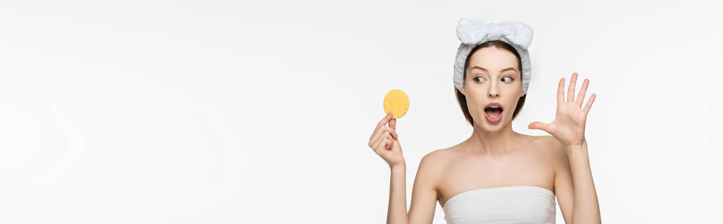 plano panorámico de chica sorprendida mostrando gesto wow mientras mira esponja cosmética aislada en blanco
 - Foto, imagen