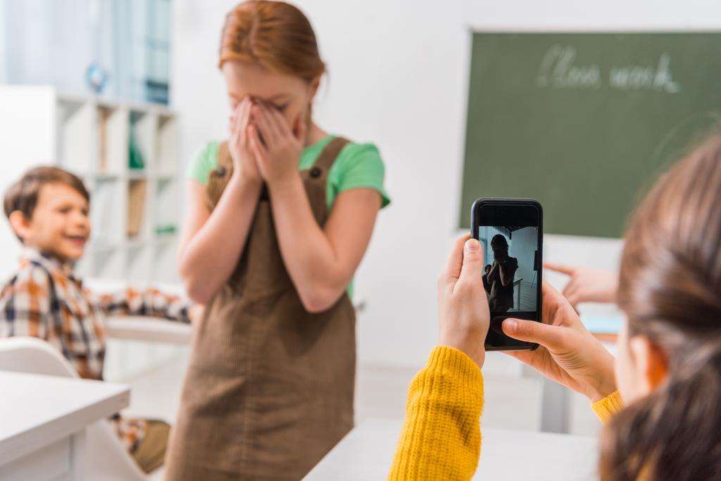 selective focus of schoolgirl taking photo of classmate, cyberbullying concept  - Photo, Image