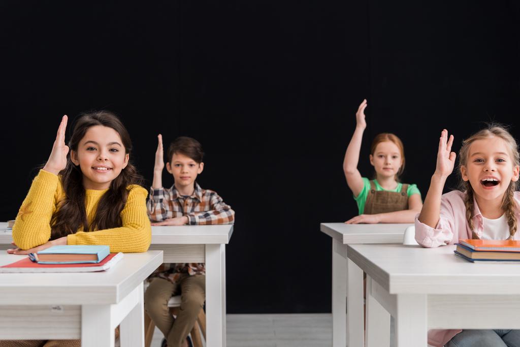selective focus of happy schoolkids with raised hands isolated on black - Photo, Image