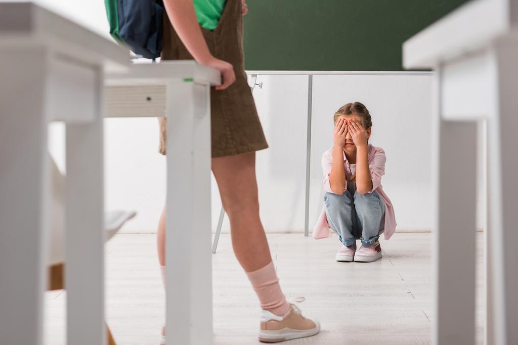 selective focus of schoolkid standing near classmate covering face while crying, bullying concept  - Photo, Image