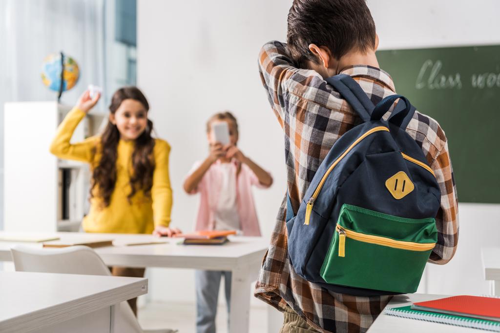 back view of bullied kid standing near cruel classmates with smartphone, cyberbullying concept  - Photo, Image