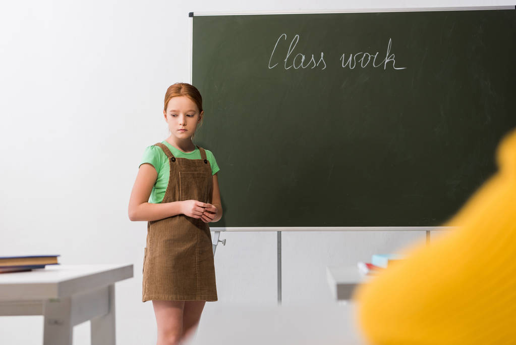 foyer sélectif de triste écolière debout près de tableau noir avec le lettrage de travail de classe
  - Photo, image