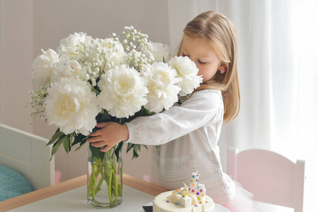 Ένα κοριτσάκι να μυρίζει ένα μπουκέτο λευκές παιώνιες. - Φωτογραφία, εικόνα