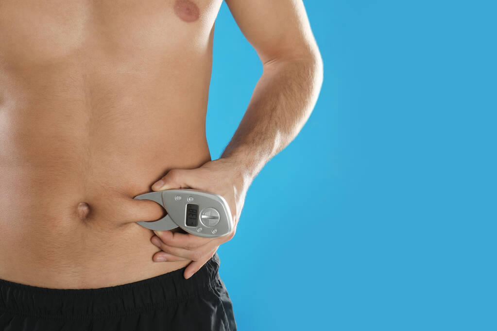Man measuring body fat layer with digital caliper on light blue background, space for text. Nutritionist's tool - Photo, Image