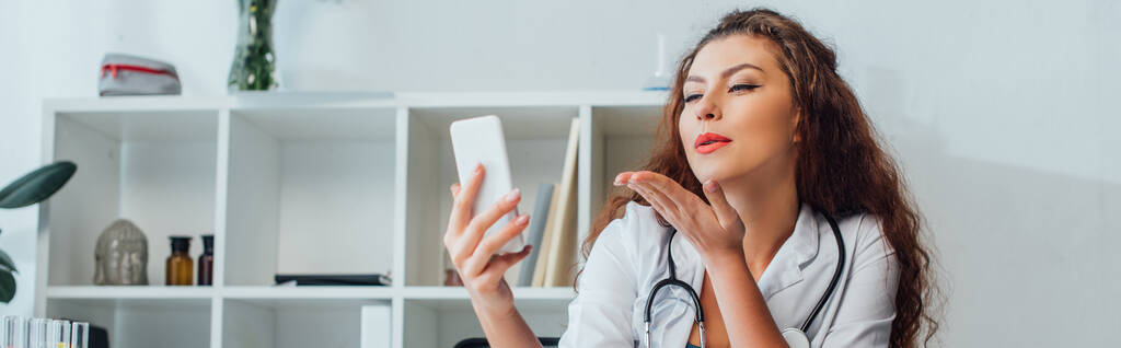 colpo panoramico di infermiera riccia e sexy che invia baci aerei mentre si scattano selfie in clinica
  - Foto, immagini