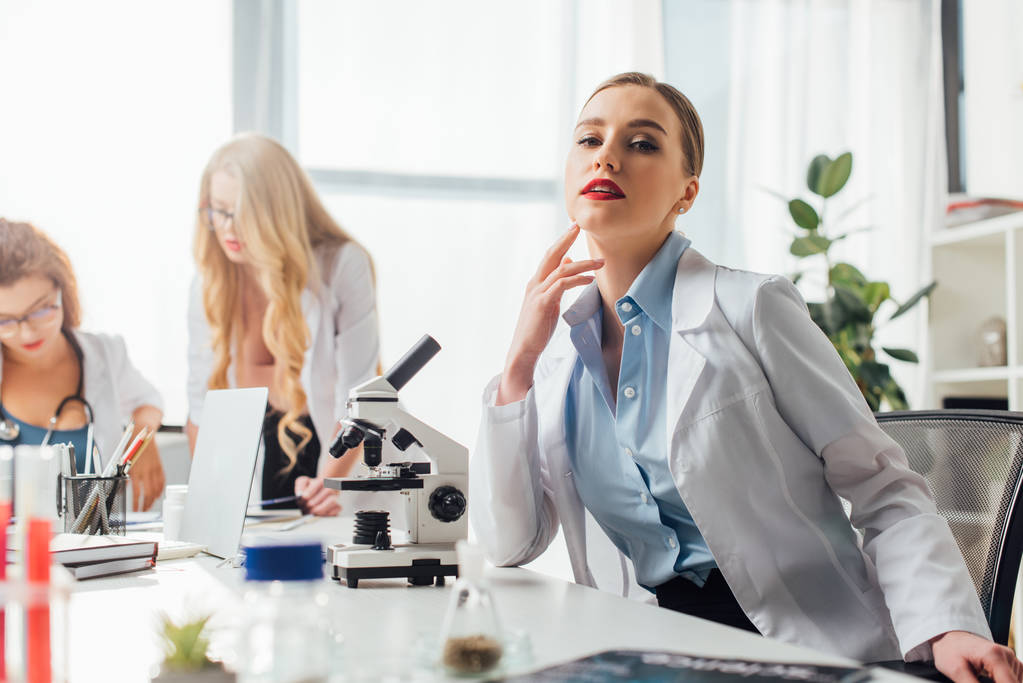 selective focus of beautiful and sexy nurse sitting near microscope and women  - Photo, Image