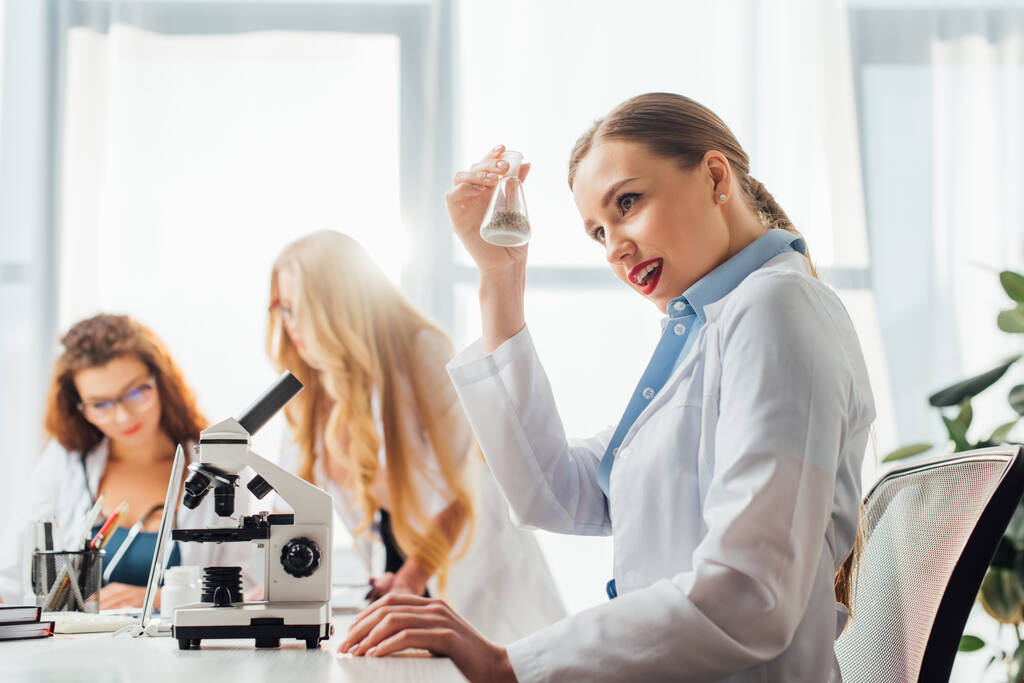 selectieve focus van mooie en sexy verpleegster holding flacon in de buurt van vrouwen in witte jassen  - Foto, afbeelding