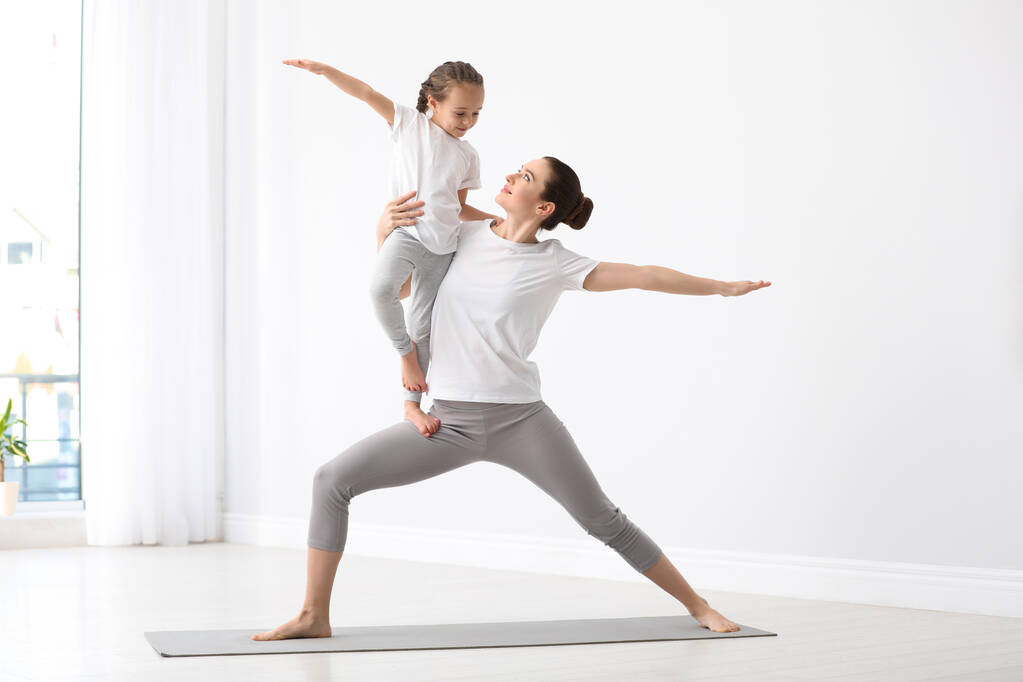 Junge Mutter mit kleiner Tochter praktiziert Yoga zu Hause - Foto, Bild