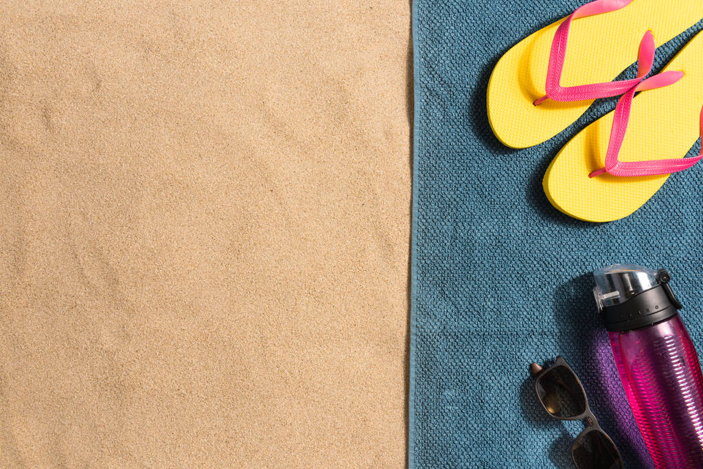 Wakacyjna kompozycja. Japonki, okulary przeciwsłoneczne i butelka wody na tle piasku. Koncepcja wakacji. Letnie tło. Surowe światło z cieniami - Zdjęcie, obraz