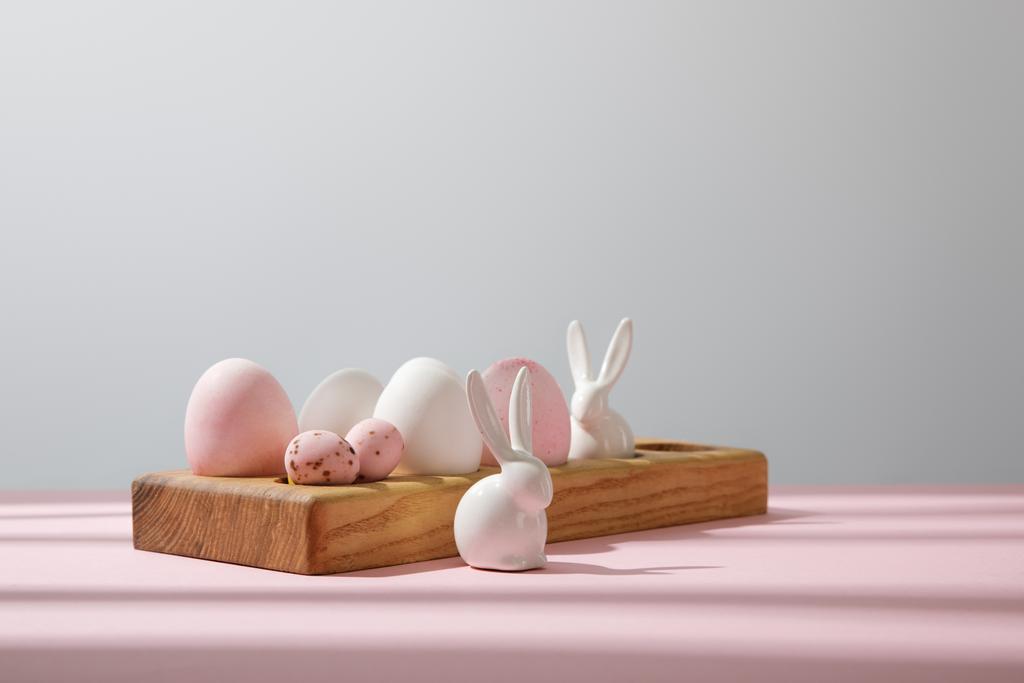 Uova di Pasqua su tavola di legno con conigli decorativi su rosa e grigio
 - Foto, immagini