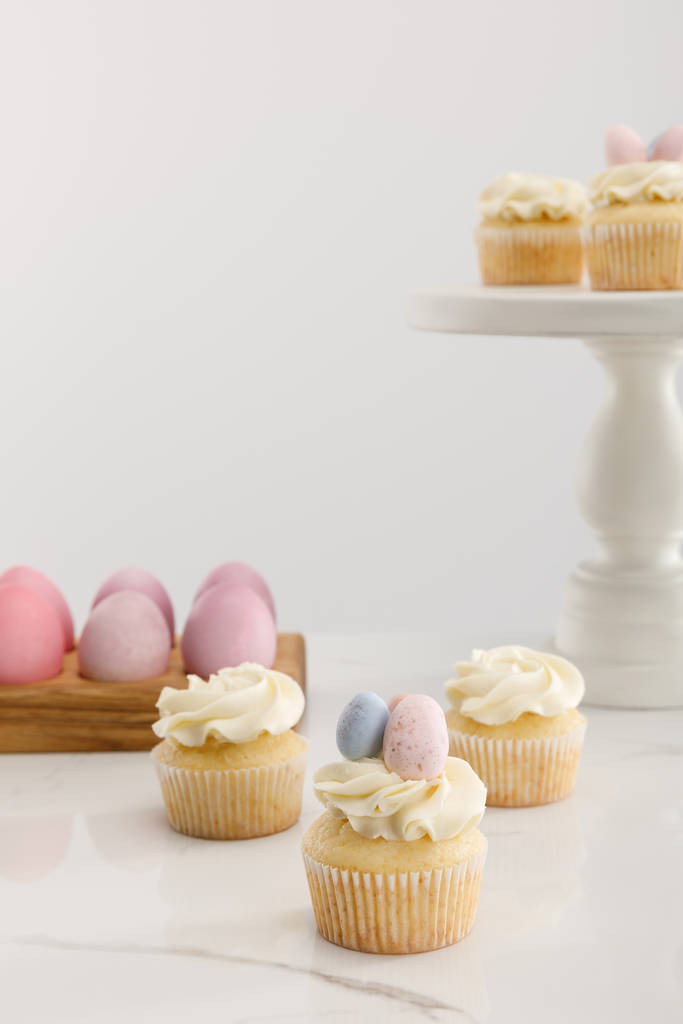 Deliciosos cupcakes de Pascua en la superficie y soporte de pastel cerca de huevos de pollo pintados sobre fondo gris
  - Foto, Imagen