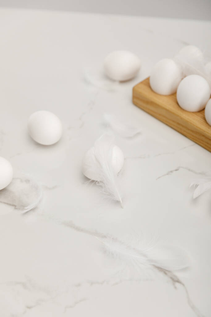 Куриные яйца на деревянной доске и перья на белом фоне
 - Фото, изображение
