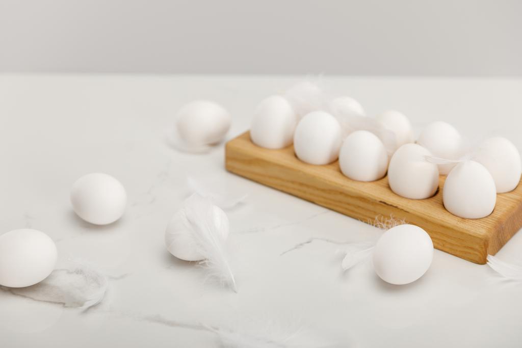 Selective focus of chicken eggs on wooden board and feathers isolated on grey - Foto, Bild
