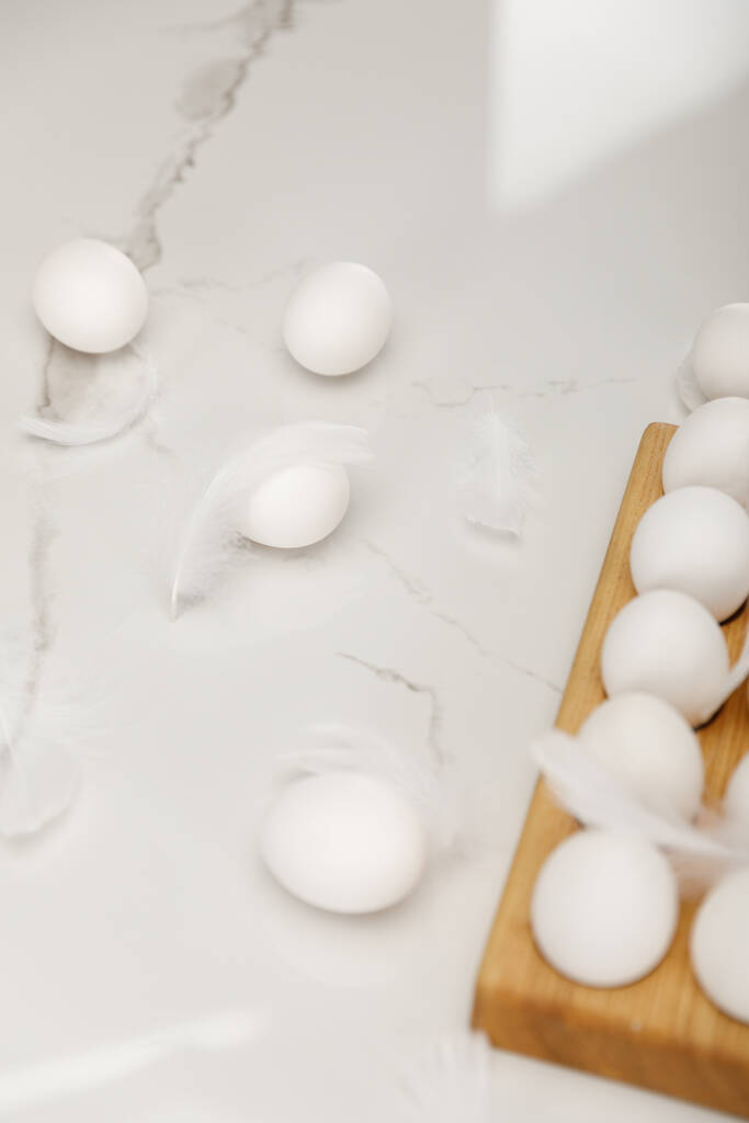 Ovos de galinha na bandeja de ovos de madeira com penas no fundo branco
 - Foto, Imagem