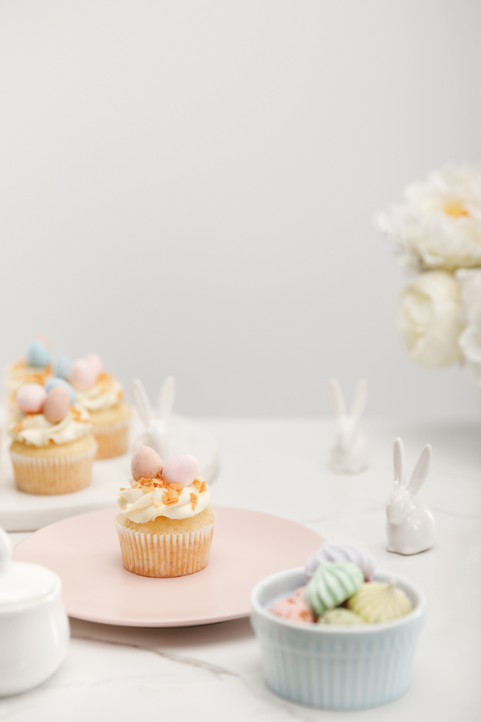 Selective focus of cupcakes with decorative bunnies, bowl with meringues and flowers on grey background - Photo, Image