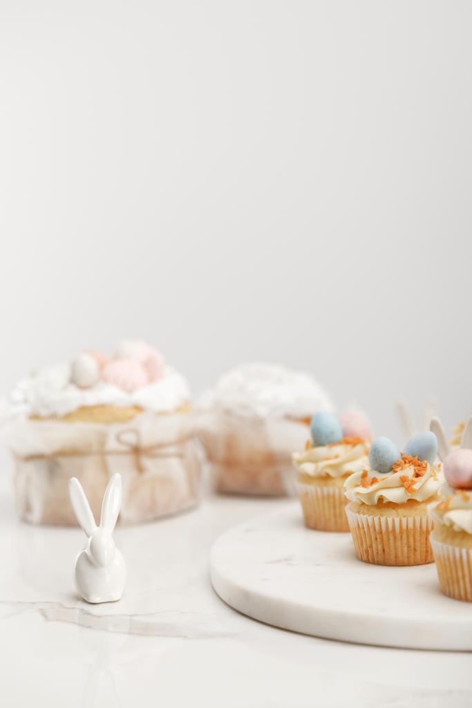 Selective focus of cupcakes on round board, decorative bunny and easter cakes on grey background - Foto, Bild