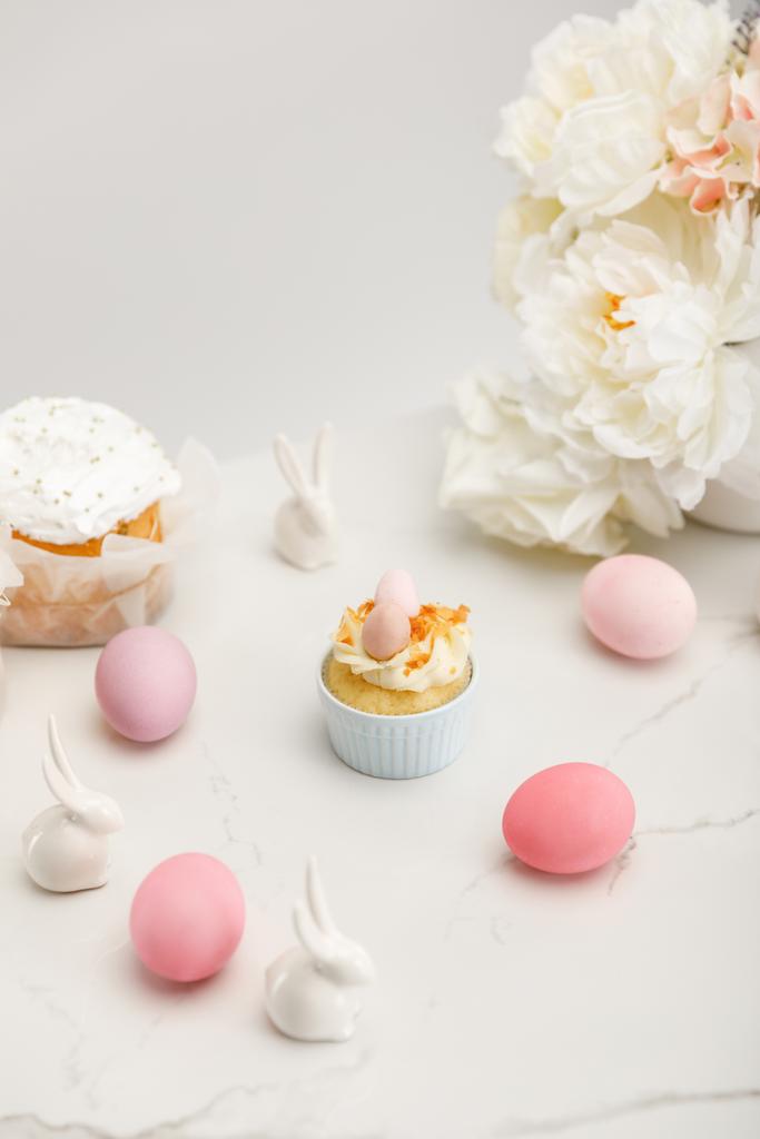Кекс з різнокольоровими курячими яйцями, декоративними кроликами, великодніми тортами та квітами на білому тлі
 - Фото, зображення