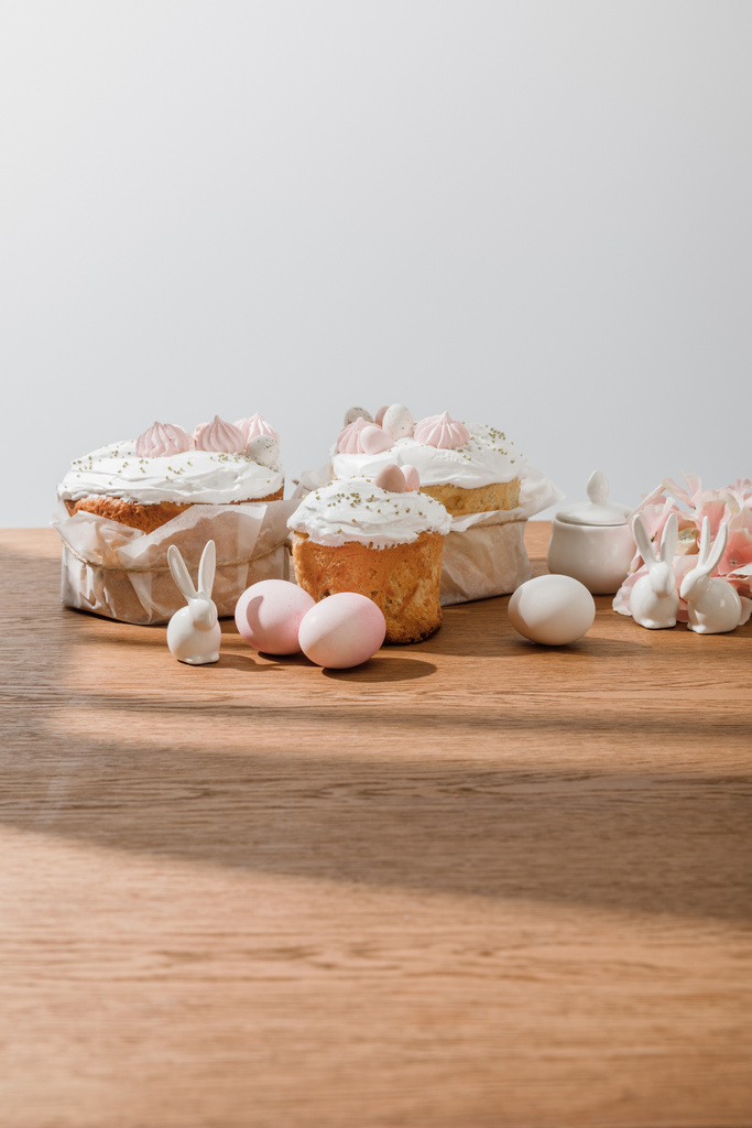Conejitos decorativos, pétalos, huevos de pollo y azucarero cerca de pasteles de Pascua aislados en gris
 - Foto, Imagen