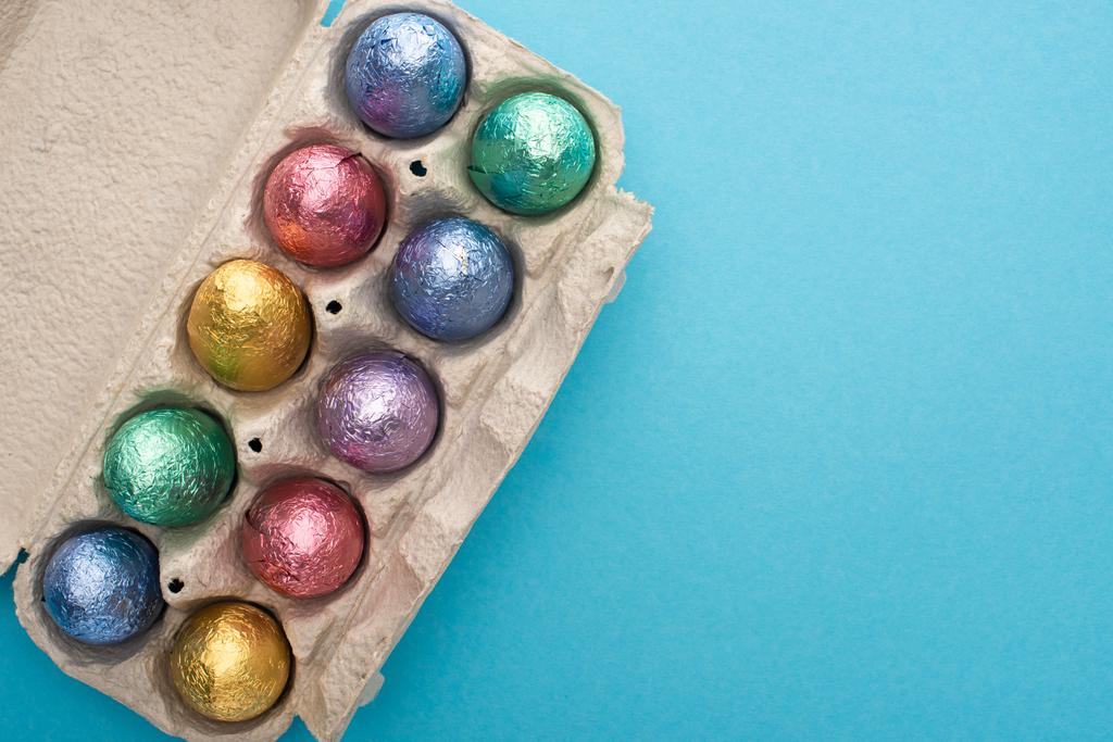 Вид зверху на шоколадні великодні яйця в яєчному лотку на синьому фоні
 - Фото, зображення