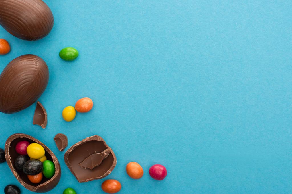 Ansicht von Schokolade Ostereier mit bunten Süßigkeiten auf blauem Hintergrund - Foto, Bild