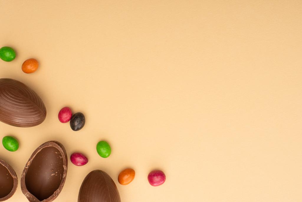 Top view of chocolate eggs and sweets on beige background - Photo, Image