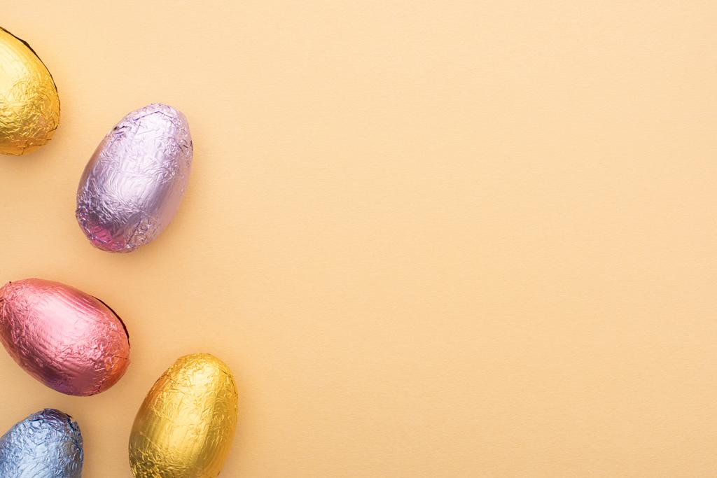 Ansicht von Schokolade-Ostereiern in bunter Folie auf beigem Hintergrund - Foto, Bild
