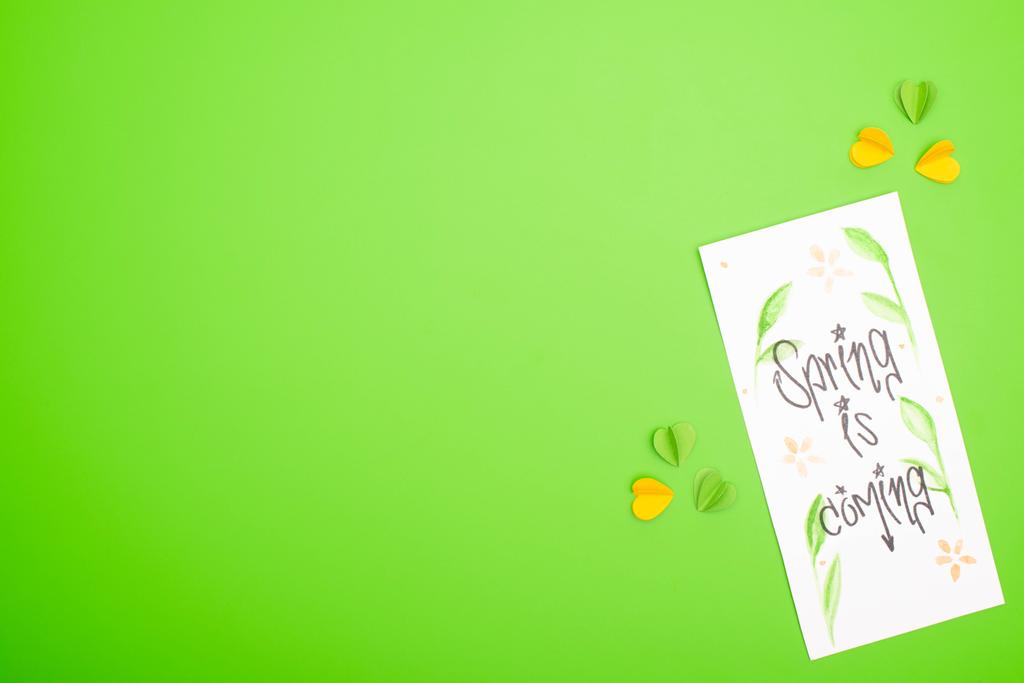 Widok z góry karty z wiosną nadchodzi liternictwo i kolorowe dekoracyjne serca na zielonym tle - Zdjęcie, obraz
