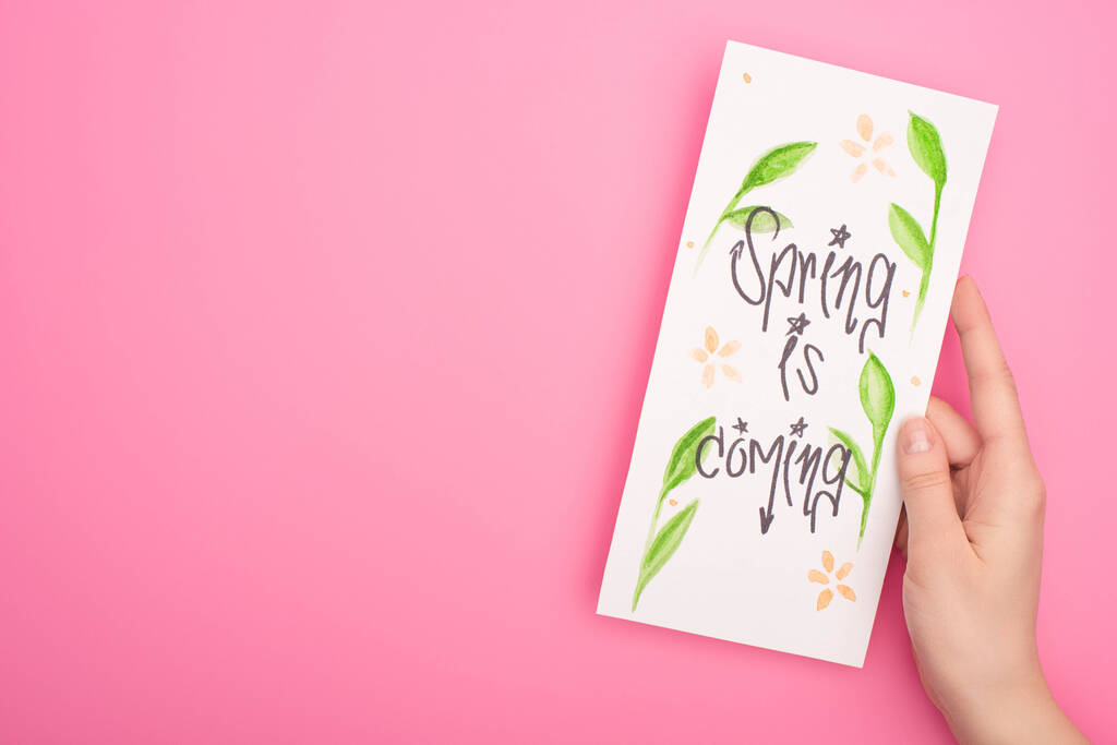 Oříznutý pohled na ženu držící kartu s jarem přichází písmo na růžovém pozadí - Fotografie, Obrázek