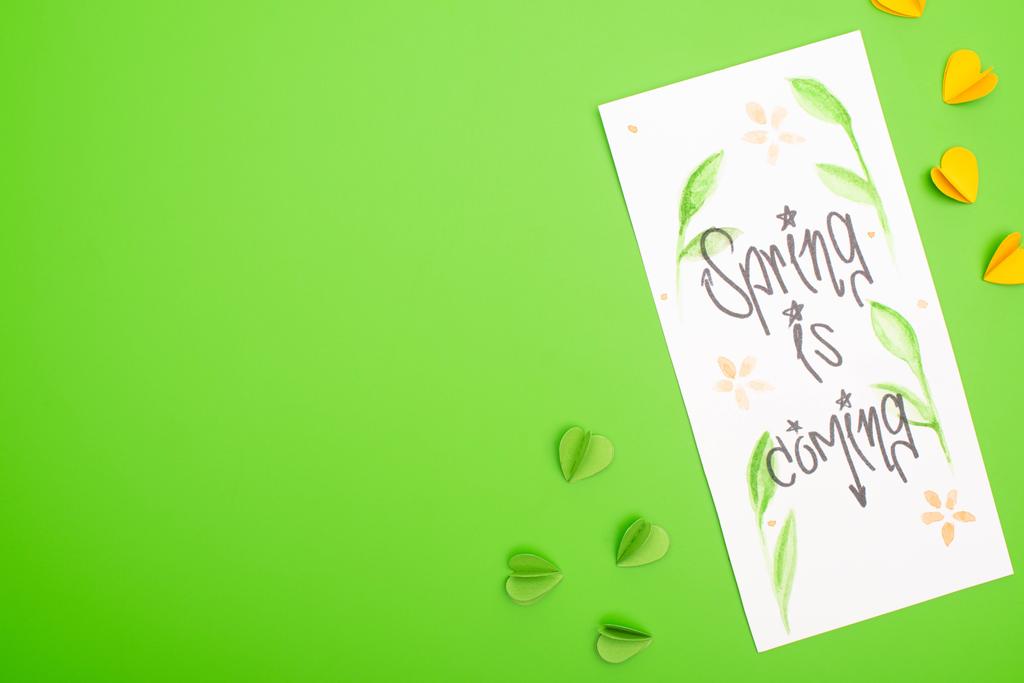 Top view of card with spring is coming lettering and decorative hearts on green background - Photo, Image