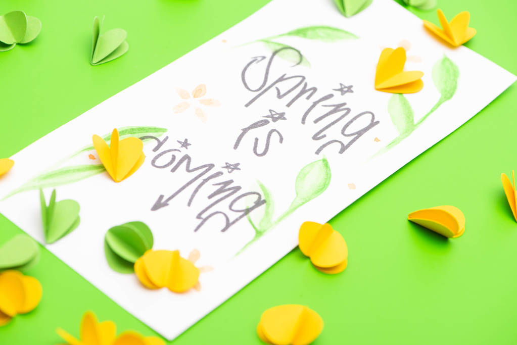Selective focus of card with spring is coming lettering and decorative hearts on green background - Photo, Image