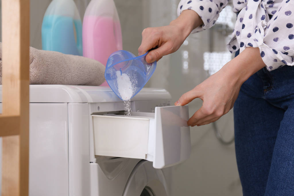 Frau gießt Waschmittel in Waschmaschinenschublade im Badezimmer, Nahaufnahme - Foto, Bild
