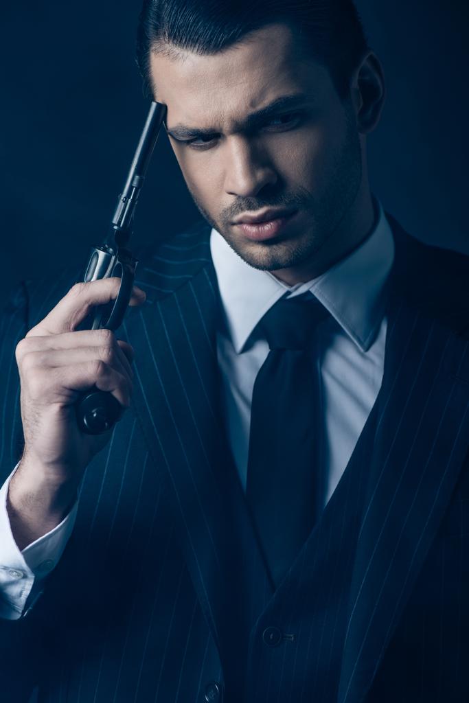 Elölnézetben gondolkodó gengszter pisztollyal sötét kék háttér - Fotó, kép